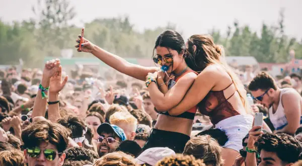 Menschen feiern ausgelassen beim **pulse open air**. Eine Frau hält ihr Handy hoch, während eine Freundin sie umarmt.