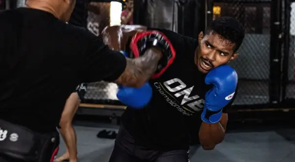 Fighter in blue gloves dodges an overhand punch during intense MMA training.