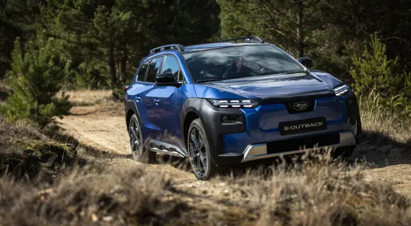 Niebieskie Subaru E-Outback pokonuje piaszczystą drogę wśród drzew. Jazda Subaru po bezdrożach.