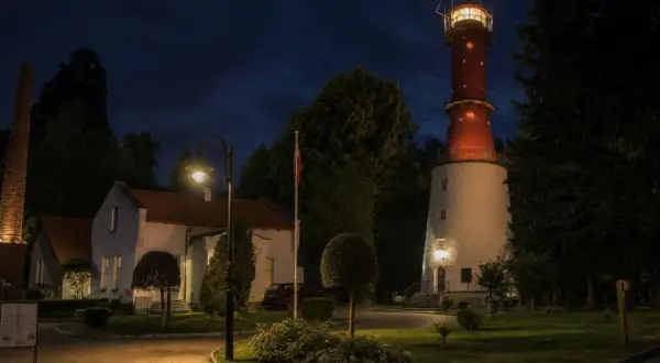 Nocna panorama z latarnią morską Rozewie, budynkami i ceglanym kominem.