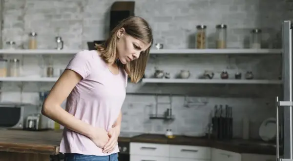 Kobieta w kuchni trzyma się za brzuch, odczuwając ból. Może to być jeden z objawów chlamydii.