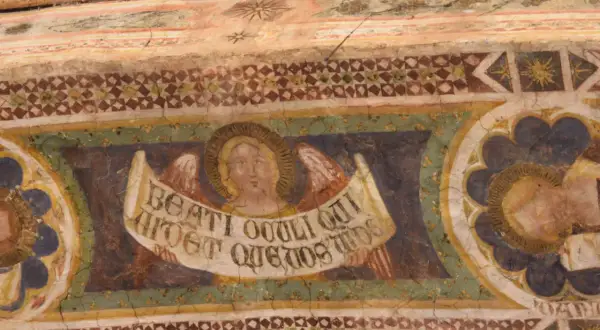 Angeli con pergamena negli affreschi dell'abbazia di Pomposa. Dettaglio di un volto angelico con ali e iscrizione latina, parte di un ciclo pittorico antico.