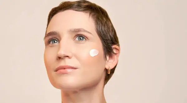 Une femme au regard pensif, avec une touche de crème solaire avant ou après crème hydratante sur la joue.