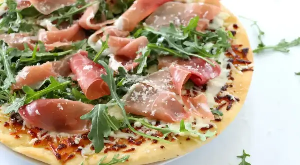 Pyszna pizza prosciutto z rukolą i parmezanem, idealna na letni wieczór.