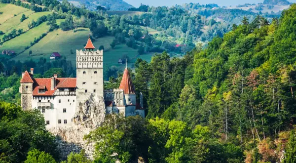 Zamek Bran w Rumunii na tle zielonych wzgórz i lasów.