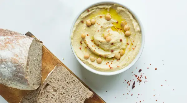 Misternie ułożony hummus z ciecierzycą i oliwą, obok chleba. Czy hummus ma dużo białka? Tak, to świetne źródło!