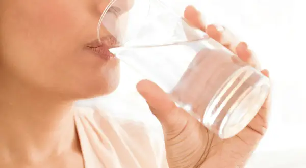 Une personne boit un verre d'eau, un geste simple pour savoir comment bien s'hydrater et rester en forme.