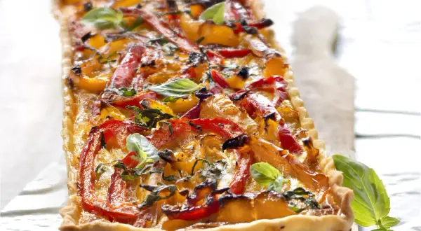 Tarte rectangulaire aux poivrons rouges et jaunes grillés, garnie de basilic frais. Un délice coloré et savoureux.