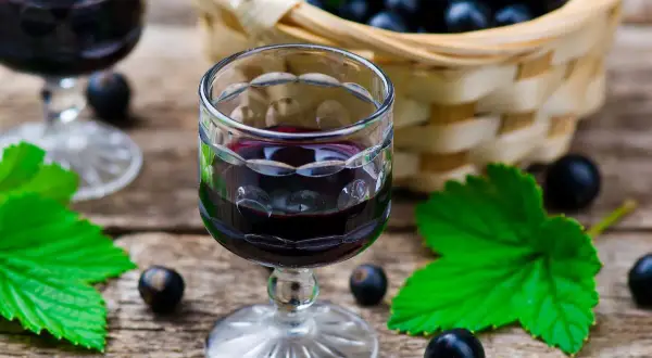 W kieliszku wino z porzeczek czarnych, obok koszyk pełen owoców i liście.
