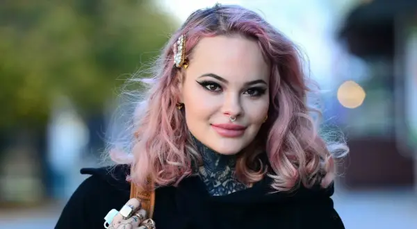 Monika Miller z różowymi włosami i tatuażami na szyi, mimo choroby, uśmiecha się do obiektywu.