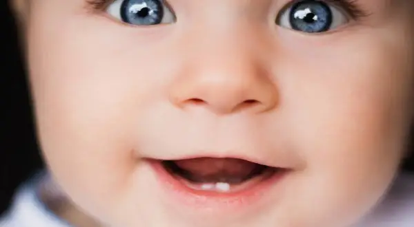 Occhi azzurri e un sorriso che promette gioia in questa vista neonati. Un piccolo dente spunta, segno di crescita.