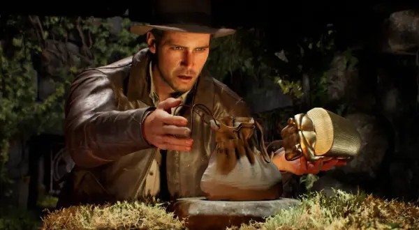 Indiana Jones i wielki krąg: archeolog z kapeluszem i skórzaną kurtką ostrożnie podnosi złoty artefakt w kształcie skarabeusza, obok leży skórzana sakiewka.