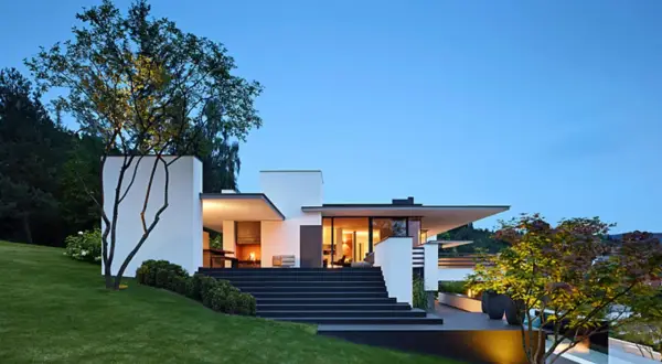 Moderne Villa mit breiter, dunkler Treppe zum Hauseingang. Tolle Ideen für Haus und Treppe, beleuchtet bei Dämmerung.