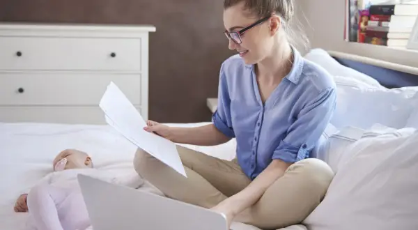 Kobieta na macierzyńskim pracuje przy laptopie, podczas gdy dziecko śpi obok.