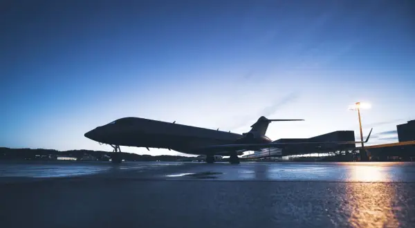 Ein Privatjet steht auf einem nassen Rollfeld bei Dämmerung.