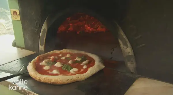 Eine authentische Pizza Napoletana mit Mozzarella und Basilikum wird in einem Holzofen gebacken.