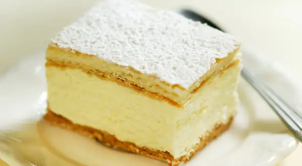 Pyszne ciasto budyniowe bez pieczenia, z kremowym nadzieniem i wafelkami, posypane cukrem pudrem.