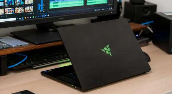 Czarny laptop Razer z podświetlanym logo, obok monitor z edytorem wideo i dysk sieciowy. Prawdopodobnie najdroższy komputer gamingowy na świecie.