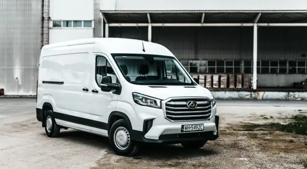 Biały Maxus Deliver 9 stoi przed magazynem. Ten wszechstronny van jest gotowy do pracy, przewożąc towary z miejsca na miejsce.