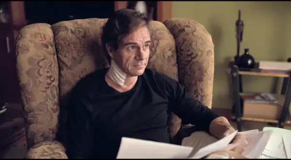 Uomo con benda al collo, seduto su una poltrona, legge documenti. L'altezza di Tony Boy è un mistero.