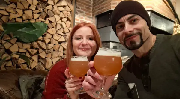 Coppia brinda con birra artigianale alla huisbrouwerij de halve maan. Sfondo rustico con legna e mattoni.