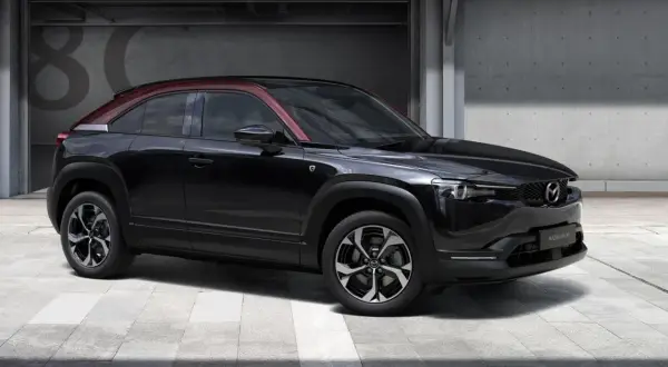 Czarna Mazda MX-30 z czerwonym dachem, prezentująca swoje kompaktowe mazda mx 30 wymiary, stoi przed betonową ścianą z numerem 80.