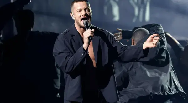 Imagine Dragons koncert Polska: wokalista Dan Reynolds śpiewa na scenie, otoczony tancerzami w mrocznym klimacie.