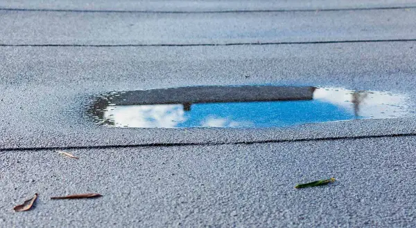 Pfützen auf der Dachpappe spiegeln den Himmel. Feuchtigkeit unter Dachpappe deutet auf ein Problem hin.