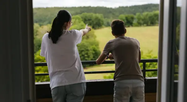 Zwei Jugendliche blicken von einem Balkon in die grüne Natur. Sie wollen raus aus der sozialen Arbeit und die Freiheit genießen.