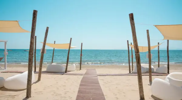Un percorso in legno conduce al mare cristallino del golfo di Follonica, tra comode sedute bianche e tende parasole.