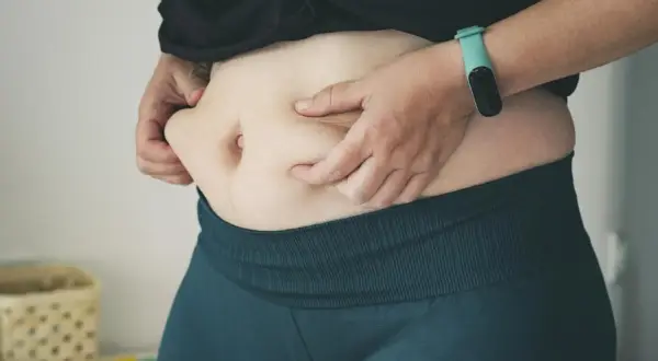 Osoba ściska fałd tłuszczu na brzuchu, zastanawiając się, ile trzeba chodzić, żeby spalić 500 kcal.