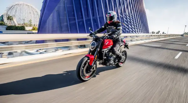 Mujer conduce moto roja por puente moderno. Con 18 años, puedes sacarte el carnet de moto A2.