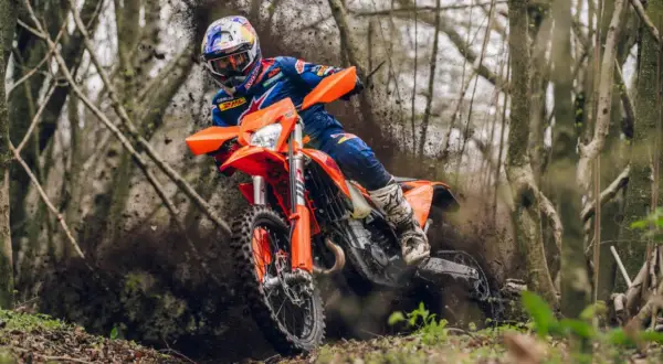 Piloto en una KTM 490 Adventure derrapando en un sendero boscoso, levantando barro.