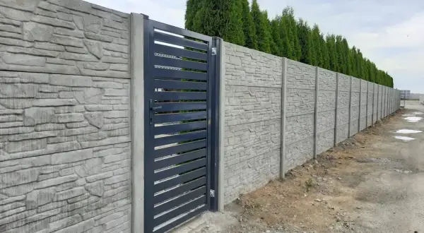 Betonowy płot z kamiennym wzorem i ciemnoszarą bramą.