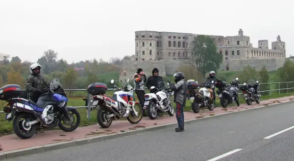 Motocykliści i ich maszyny na tle ruin zamku.