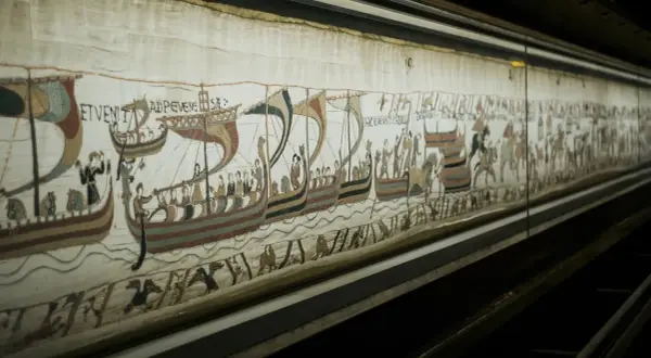 Detaljerad vy av Bayeuxtapeten på museum, med vikingaskepp och figurer som skildrar historiska händelser.