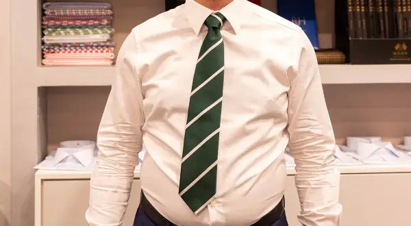 Uomo con camicia bianca e cravatta verde a righe, annodata con un elegante nodo mezzo windsor.