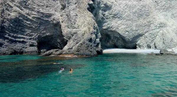 Gente nadando y haciendo snorkel en las aguas cristalinas de la cala puente Almería, rodeada de imponentes acantilados rocosos.