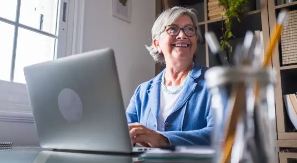 Lächelnde Frau am Laptop, die überlegt, wie sie Rente beziehen und vollzeit arbeiten kann, ohne die Steuerklasse zu ändern.