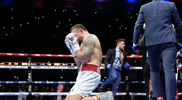 A boxer kneels in the ring, head in hands, after a tough fight. The Dubois vs Usyk bout ends with a somber moment.