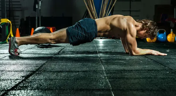 Mann im Fitnessstudio in Plank-Position, trainiert seinen Rumpf.