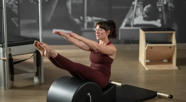 Donna in posa di equilibrio sul reformer Pilates, con le gambe sollevate e le braccia tese. Il suo sguardo concentrato esprime il **core significato** di forza e controllo.