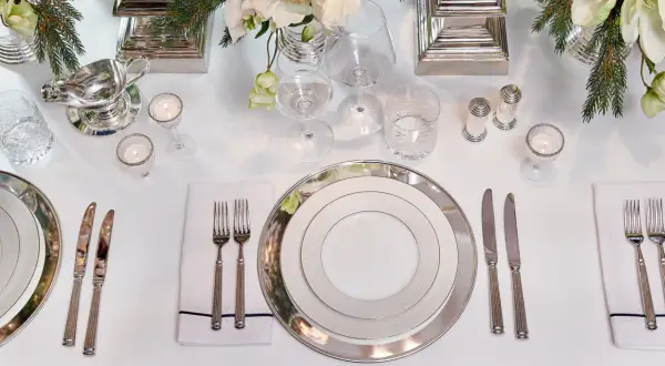 Elegant dukning med silverbestick på samma sida. Vita blommor och granris ger en festlig känsla.