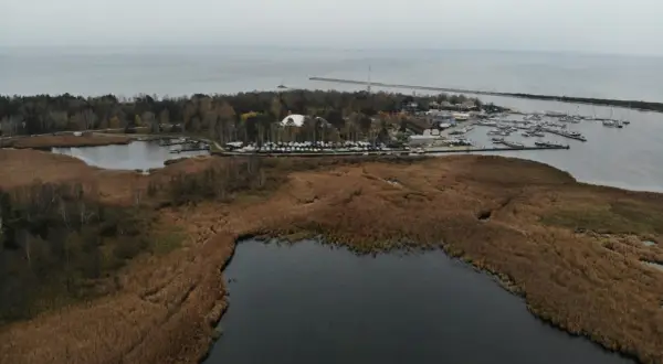 Widok na port jachtowy i jezioro otoczone trzcinami. W oddali widać morze i falochron. To malownicze **górki zachodnie**.