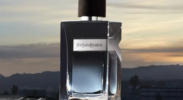 Elegancka butelka Y Yves Saint Laurent Y 100ml na tle zachodzącego słońca nad miastem.