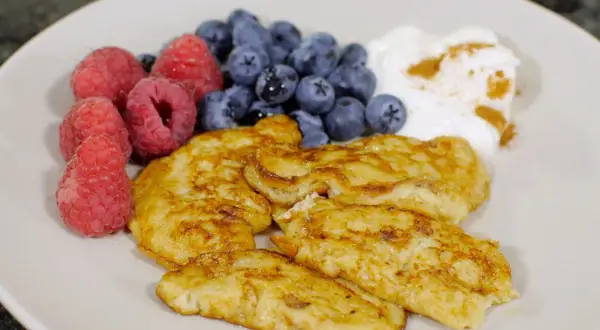 En tallrik med gyllene pannkakor, färska hallon, blåbär och en klick yoghurt med kanel. Perfekt för diabetes mat recept.