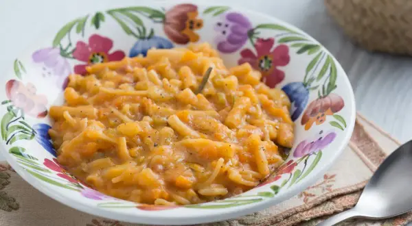 Un plat réconfortant de pâtes italiennes avec de la pomme de terre et des légumes, servi dans un bol fleuri.