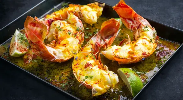 Langoustes grillées dans un plat avec du citron vert et des herbes.