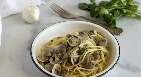 Un piatto invitante di linguine alle vongole, con aglio e prezzemolo freschi sullo sfondo.