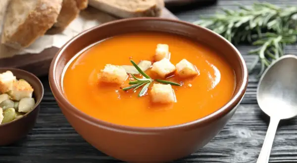Aksamitny zupa krem z batatów, udekorowana grzankami i rozmarynem, podana z chlebem i pestkami dyni.